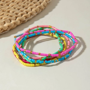 Detail of bohemian colorful heishi bead bracelets with golden spacer accents on sand background