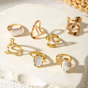 Detail of 7-piece gold pearl ring set displayed on textured white stone with warm lighting
