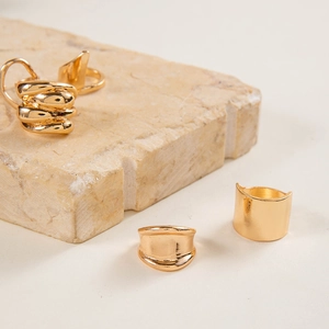 Detailed view of three gold-plated geometric rings on a minimalist stone display stand