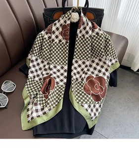 Detail of camellia and houndstooth print silk scarf draped on a black leather handbag