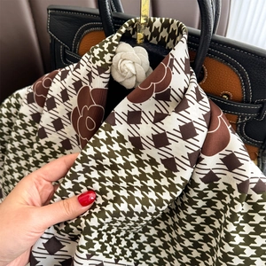Detailed texture of plaid silk scarf with camellia print draped on a leather bag