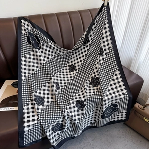 Detail of a black and white check scarf with camellia print draped over a leather sofa