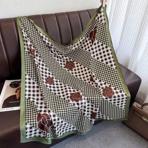 Plaid and camellia print silk square scarf elegantly draped on a brown leather sofa