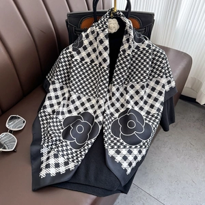 Elegant camellia and houndstooth print silk shawl draped over a black leather handbag
