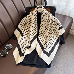 Eleganter beige Seidenschal mit schwarzem Geometriemuster an einer schicken Ledertasche