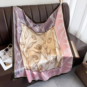 Satin floral silk square scarf with purple and beige tulip patterns on leather sofa
