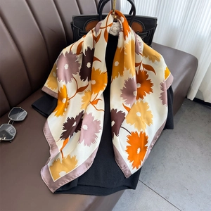 Floral print silk scarf featuring sunflower patterns draped over a bag on a sofa