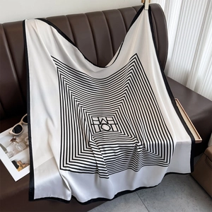 Elegant silk-like square scarf with black and white geometric patterns on a leather sofa