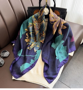 Detail of silk-satin scarf with purple lotus print draped on white knitwear and black handbag