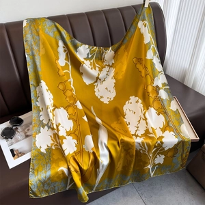 Mustard yellow silk scarf with white floral print draped on a leather sofa