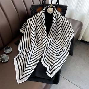 Elegant black and white striped satin silk scarf displayed on a luxury leather surface
