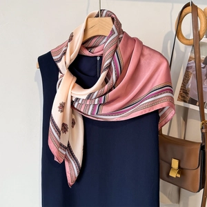 Floral faux silk neck scarf in pink and cream hanging on a blue top with a leather bag