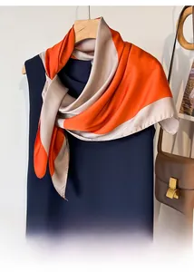 Detail of elegant orange and beige silk scarf draped on a dress with a leather bag