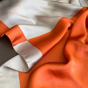 Close-up of vibrant orange and silver-grey silk scarf showing premium fabric texture
