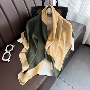 Green and gold 90cm silk square scarf elegantly draped on a leather sofa with accessories