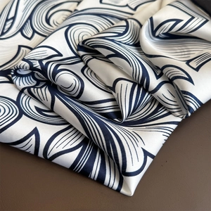 Elegant satin silk scarf with navy abstract floral print folded on leather background