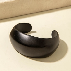 Minimalist matte black wide cuff bangle with open geometric design on a textured stone base