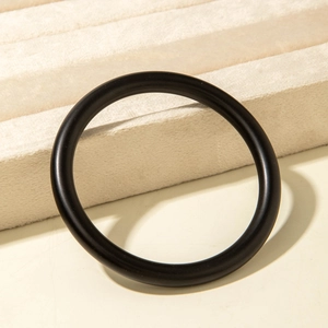 Detail view of a minimalist black matte acrylic bangle on a beige velvet jewelry display