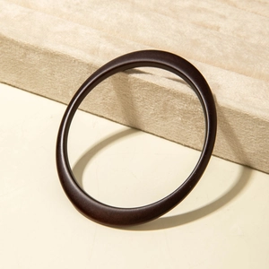 Detailed view of dark brown acrylic bangle with smooth wood grain texture on display