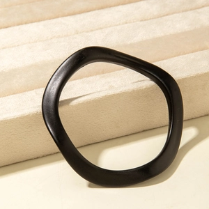 Macro detail of a minimalist black wavy acrylic bangle on a soft beige jewelry display