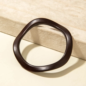 Detailed view of a dark coffee irregular wave-shaped acrylic bangle on a velvet display