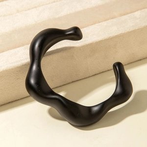 Close-up of matte black irregular wave-shaped acrylic bracelet on beige velvet stand
