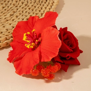 Détail de pince à cheveux fleurie en tissu rouge avec hibiscus et rose sur fond de paille