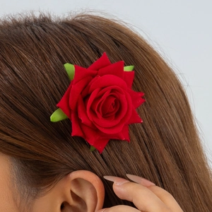 Detail shot of a deep red silk rose hair clip with green leaves worn on brown hair