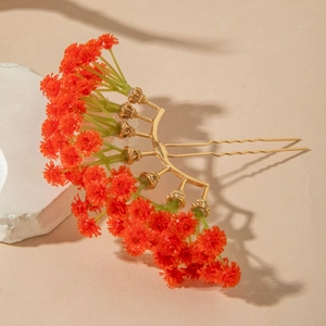 Close-up of bohemian orange floral hair comb with golden pins on a textured stone base