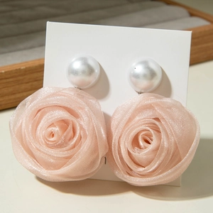 Détail de boucles d'oreilles rose en tissu avec un grand clou en perle blanche sur carte