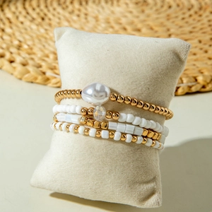 Ensemble de quatre bracelets perlés or et blanc avec une perle baroque sur un coussin beige