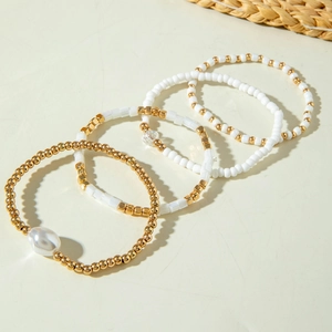 Lot de quatre bracelets extensibles avec perles dorées et perles baroques sur fond blanc