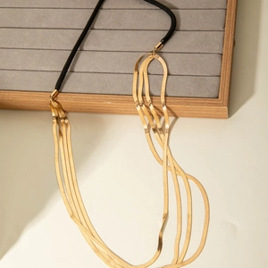 Three-layer golden flat snake chain necklace with black cord accent on velvet jewelry tray