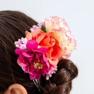 Detail of floral hair comb with pink and orange faux roses on a model's hairstyle