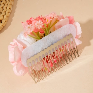 Detail of pink and white artificial floral hair comb with golden metal teeth and green leaves