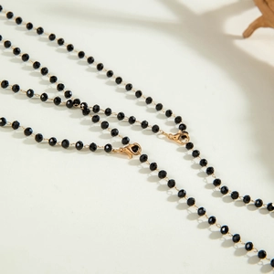 Detail of minimalist black beaded necklace with a gold lobster clasp on white background