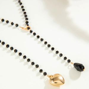 Detail of beaded tassel necklace featuring black faceted beads and a gold heart pendant