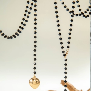 Macro shot of long beaded necklace featuring a polished gold heart pendant with black beads