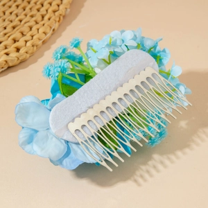 Détail d'un peigne à cheveux avec fleurs en tissu bleu clair et dents en métal argenté