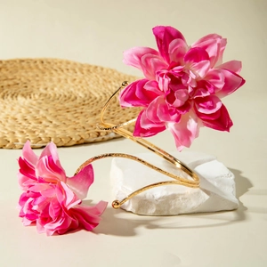 Detailaufnahme von rosa Stoffblumen an einer goldenen Armspange vor natürlichem Hintergrund