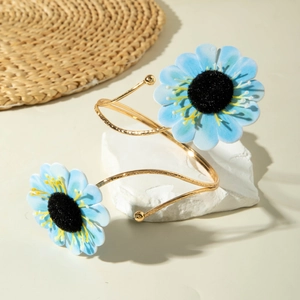 Detail eines goldenen Spiral-Armreifs mit zarten hellblauen Stoff-Sonnenblumen