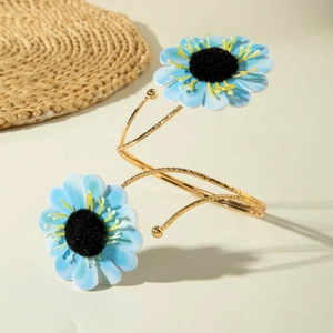 Detail eines goldenen Spiral-Armreifs mit blauen Stoffblumen und schwarzen Blütenkernen