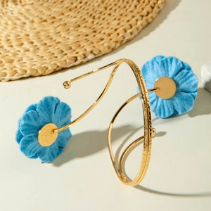 Detailansicht eines spiralförmigen goldenen Armreifs mit blauen Stoffblumen und Textur