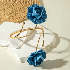 Detail eines goldenen Armreifs mit denimblauen Stoffblumen auf Steindekorationen