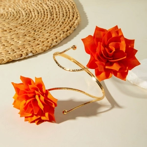 Detail eines goldenen Spiral-Armreifs mit leuchtend orangen Stoffrosen auf beigem Grund