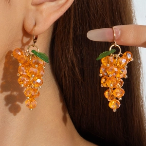 Close-up of dangling orange grape cluster earrings with green leaf detail on a model