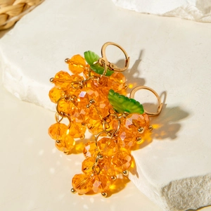 Detailed view of orange beaded grape earrings with green leaves on a stone display