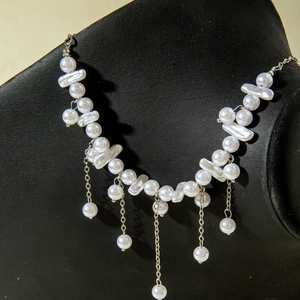 Elegant irregular pearl necklace with layered silver tassels on a black jewelry stand