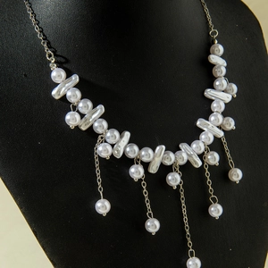 Detail of baroque pearl necklace featuring silver metal chain tassels on a black display