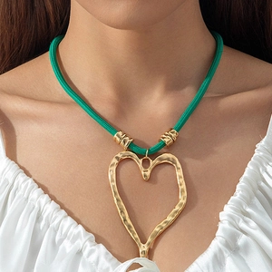 Detail of large gold heart pendant with hammered texture on a vibrant green braided cord